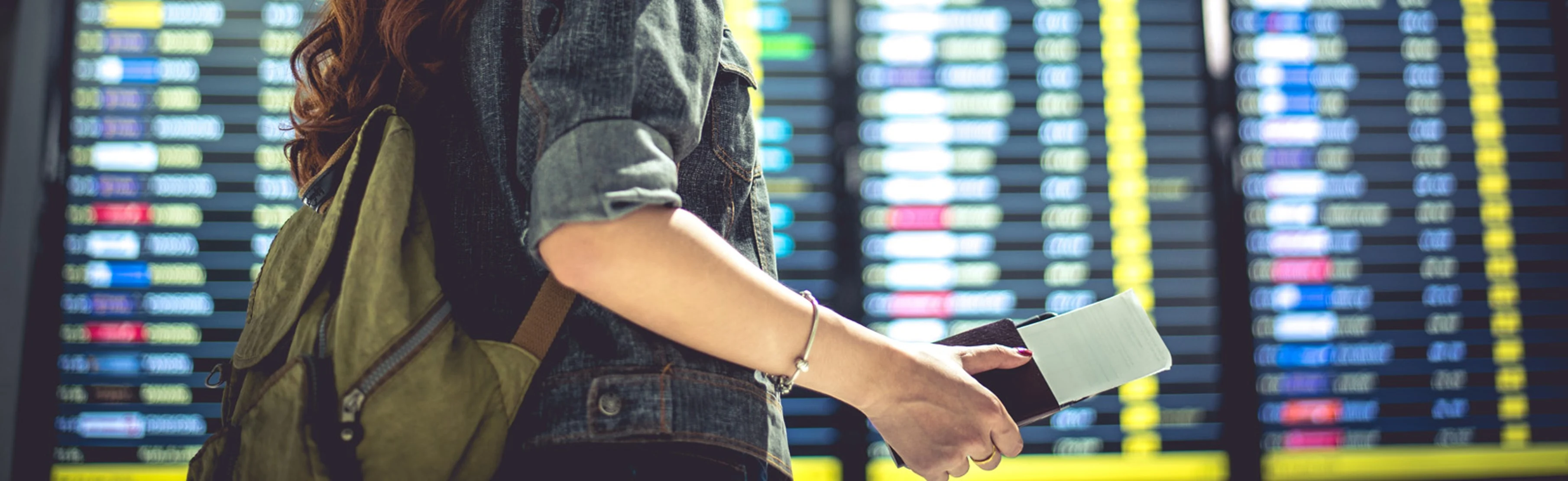 Woman holding passport in front of airport information board for Government Revenue Solutions