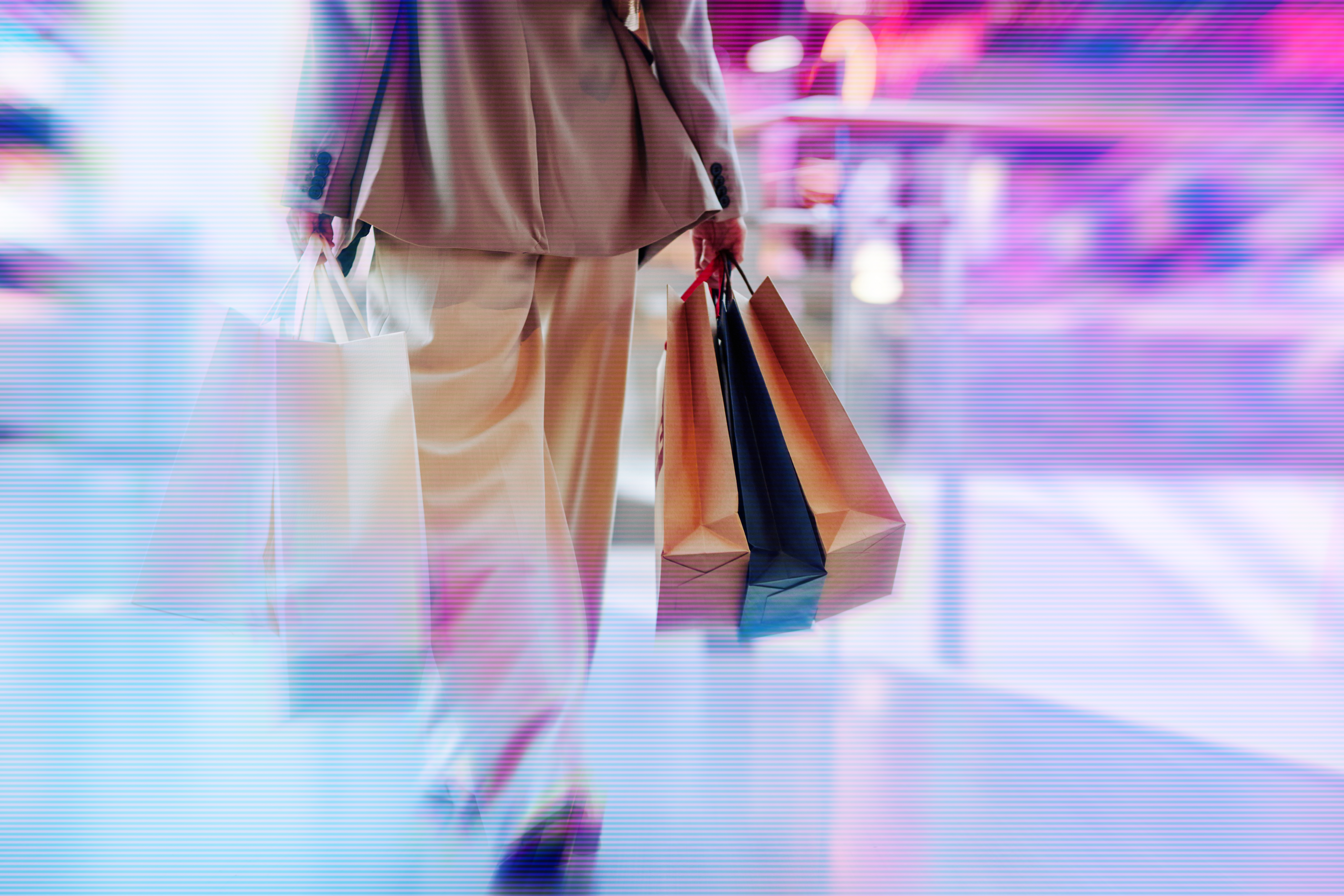 Back view of a woman carrying shopping bags while walking through a shopping centre, representing consumer activity